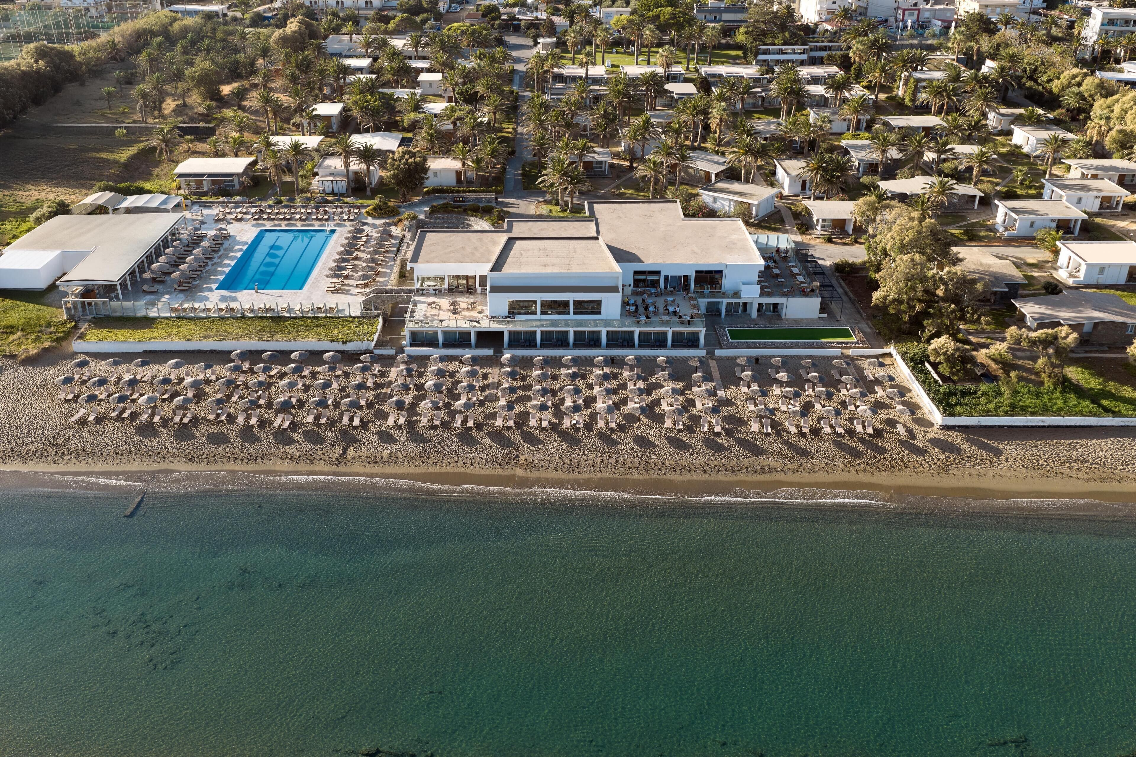 Vista aérea de un resort con una piscina grande, varias edificaciones y una zona de playa.