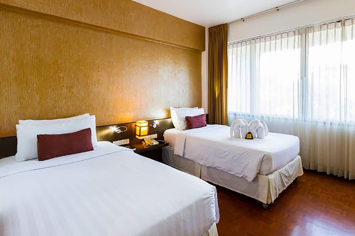 Une chambre d’hôtel avec deux lits, une table de chevet avec une lampe et une fenêtre avec des rideaux.