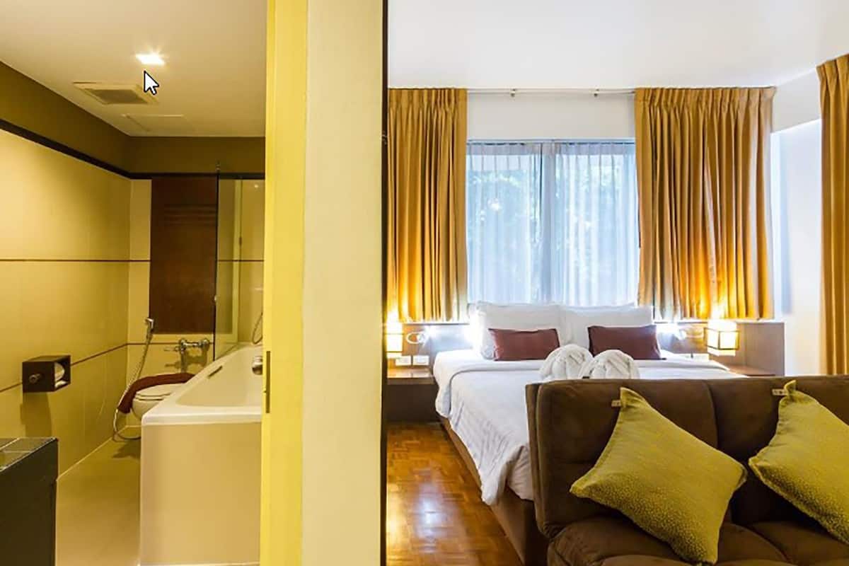 Une chambre d’hôtel avec une baignoire, un lit avec des oreillers et un canapé marron.
