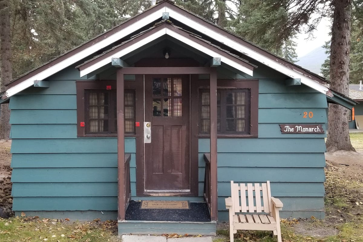A small, single-story cabin with a dark brown door, a small porch, and a bench outside.