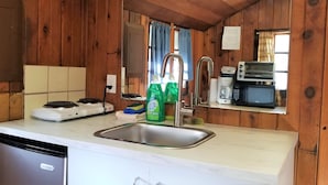 A compact kitchen with wooden walls, a sink, a stove, a microwave, and a toaster.