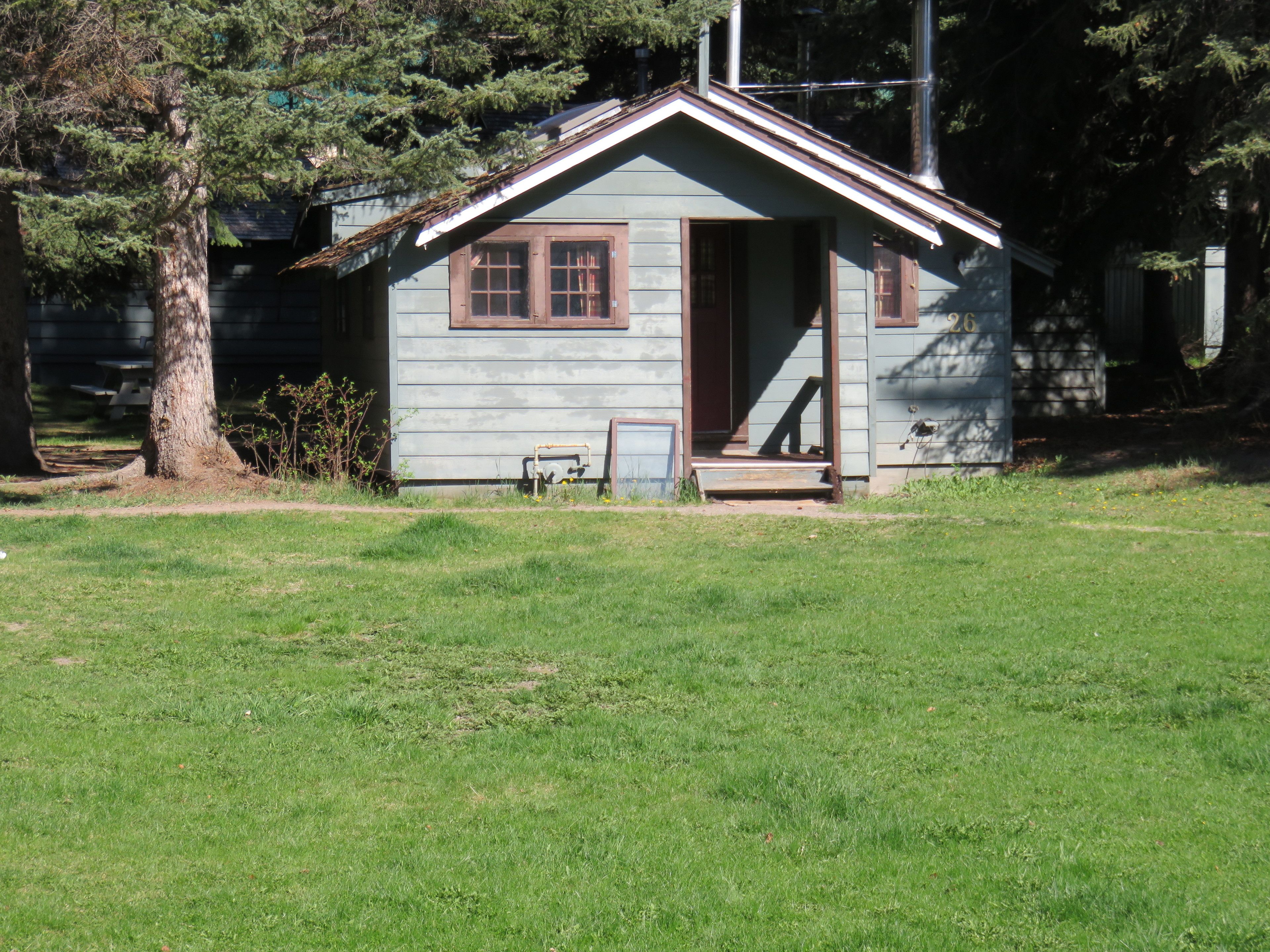 A small, single-story cabin with a gabled roof, a front porch, and a small front yard.
