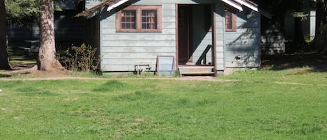 A small, single-story cabin with a gabled roof, a front porch, and a small front yard.