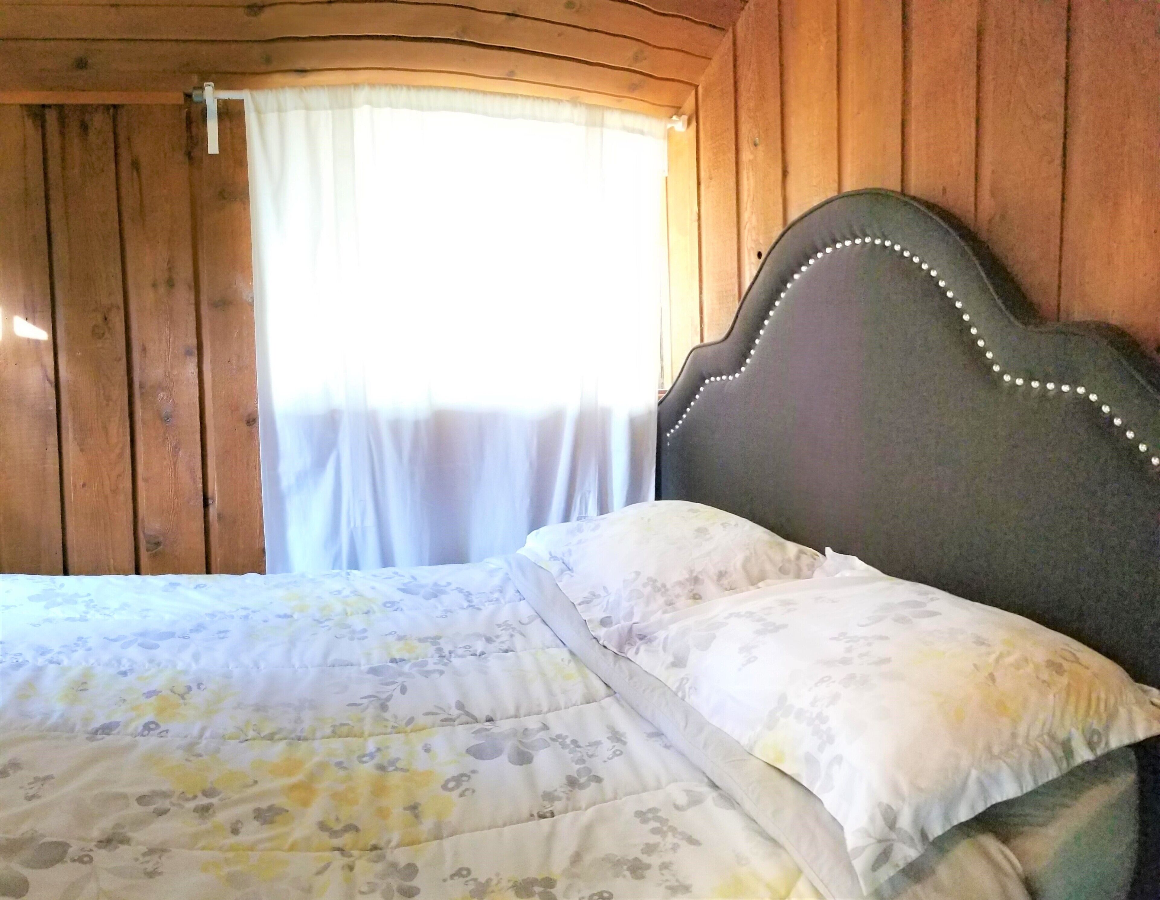 A wooden cabin bedroom with a bed featuring a floral bedspread and a headboard with bead trim.
