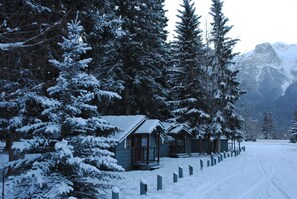 A snow-covered lodge with multiple cabins, surrounded by tall evergreen trees and mountains in the background. - Rundle Chalets (Harvie Heights)