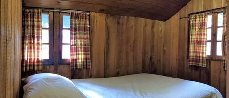A wooden cabin room with a single bed, plaid curtains, and a sloped ceiling.