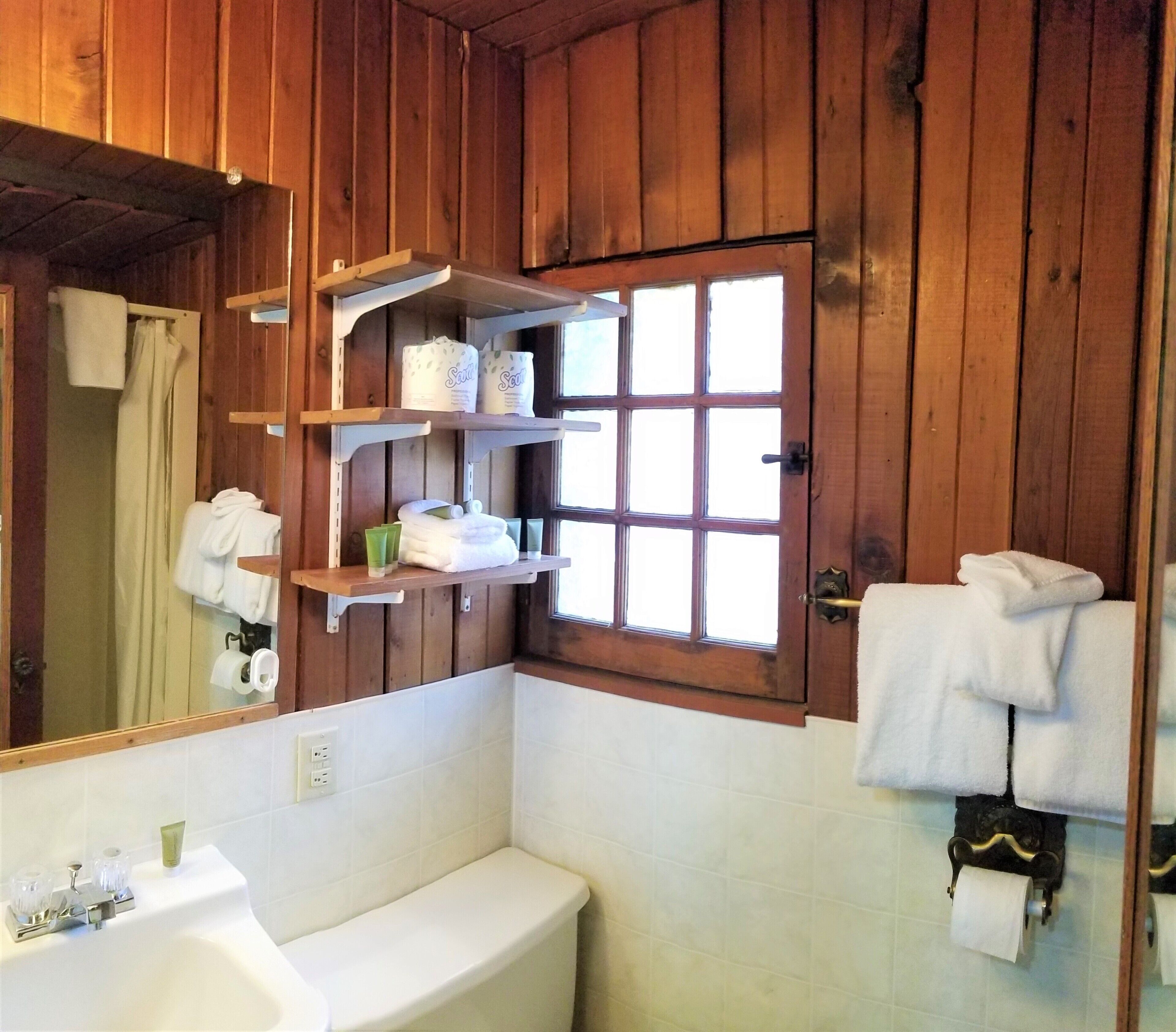 Een badkamer met houten wanden, een witte wastafel en planken met toiletartikelen.