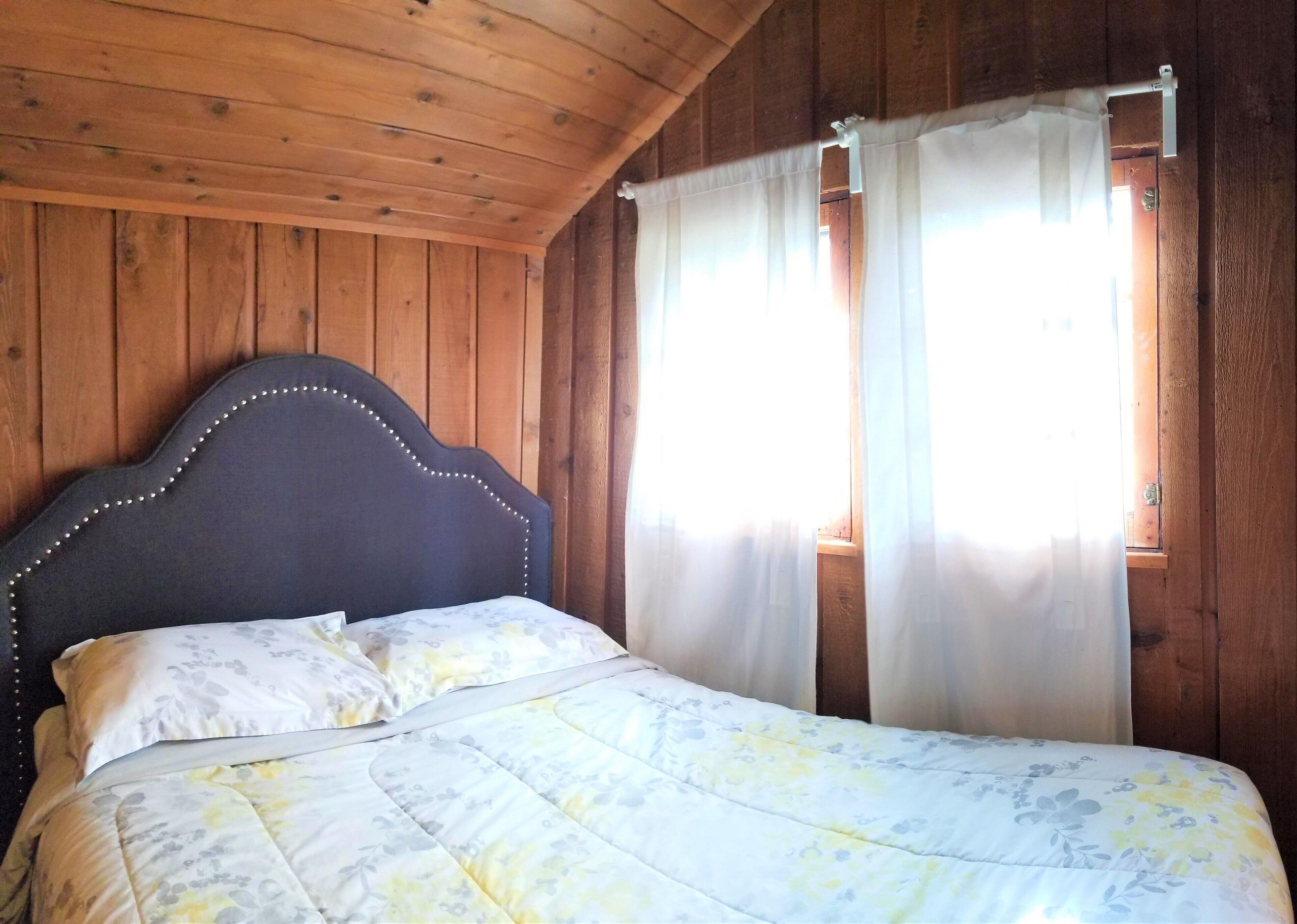 Una habitación de cabaña de madera con cama, cortinas y ventana.