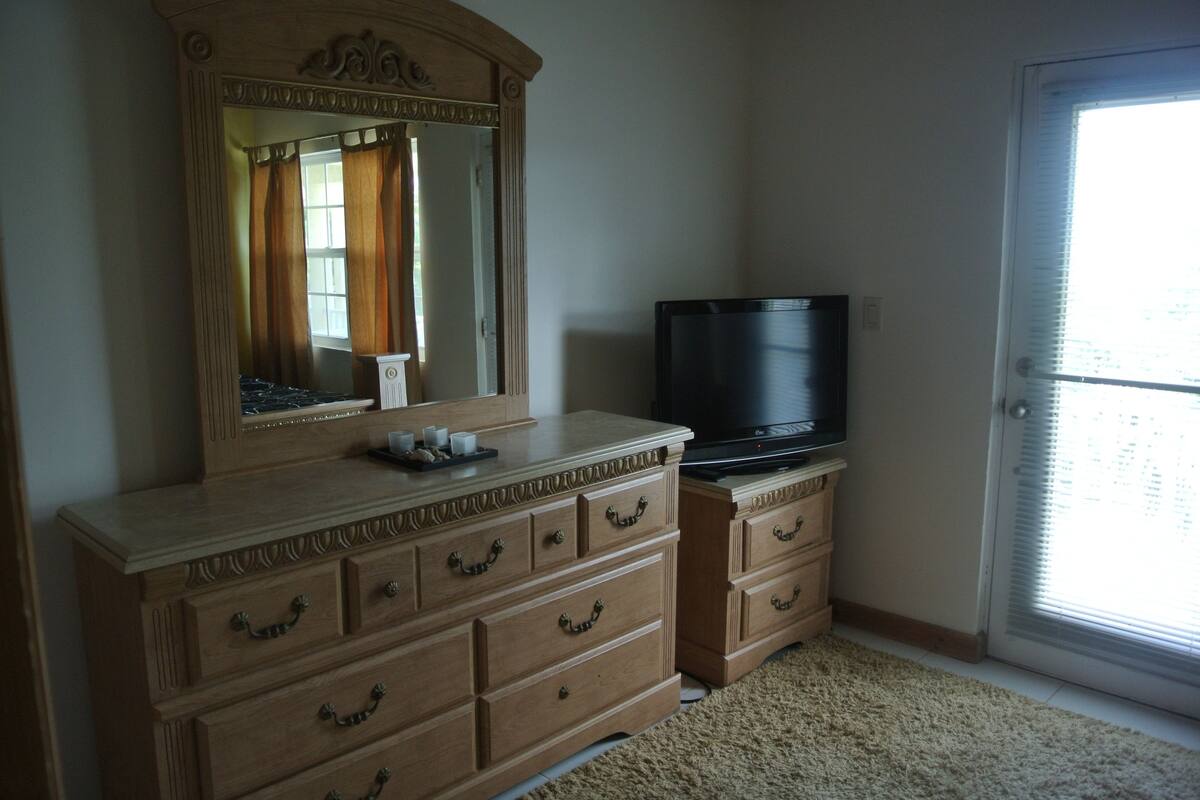 A room with a wooden dresser, a television, and a large mirror.