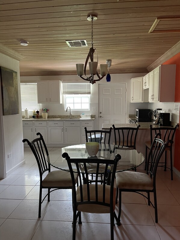A modern kitchen with white cabinets, a central island, and a dining area with chairs. - Sapphire Garden Townhouses (George Town)