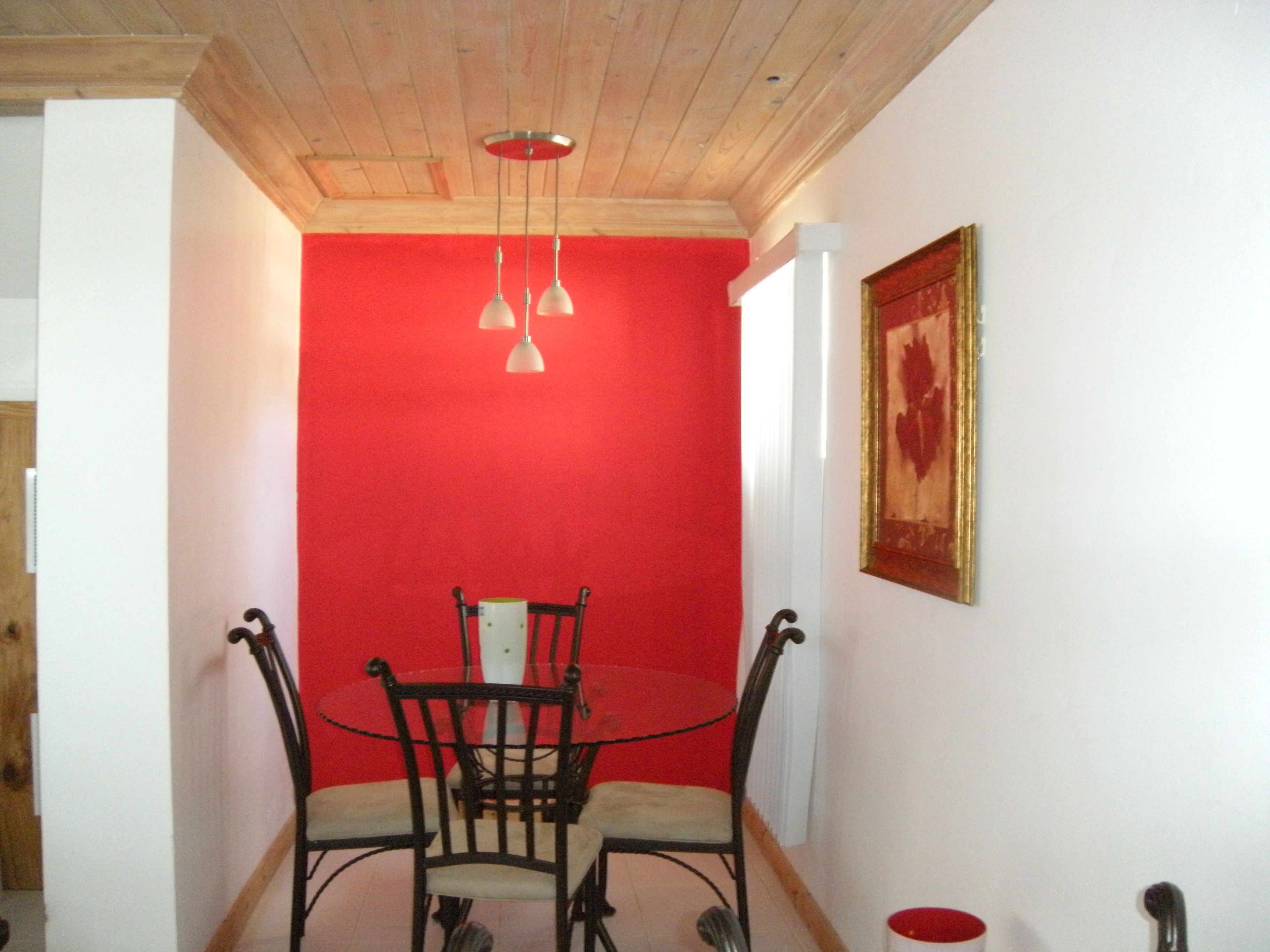 Un comedor con pared roja, techo de madera y una mesa con cuatro sillas.
