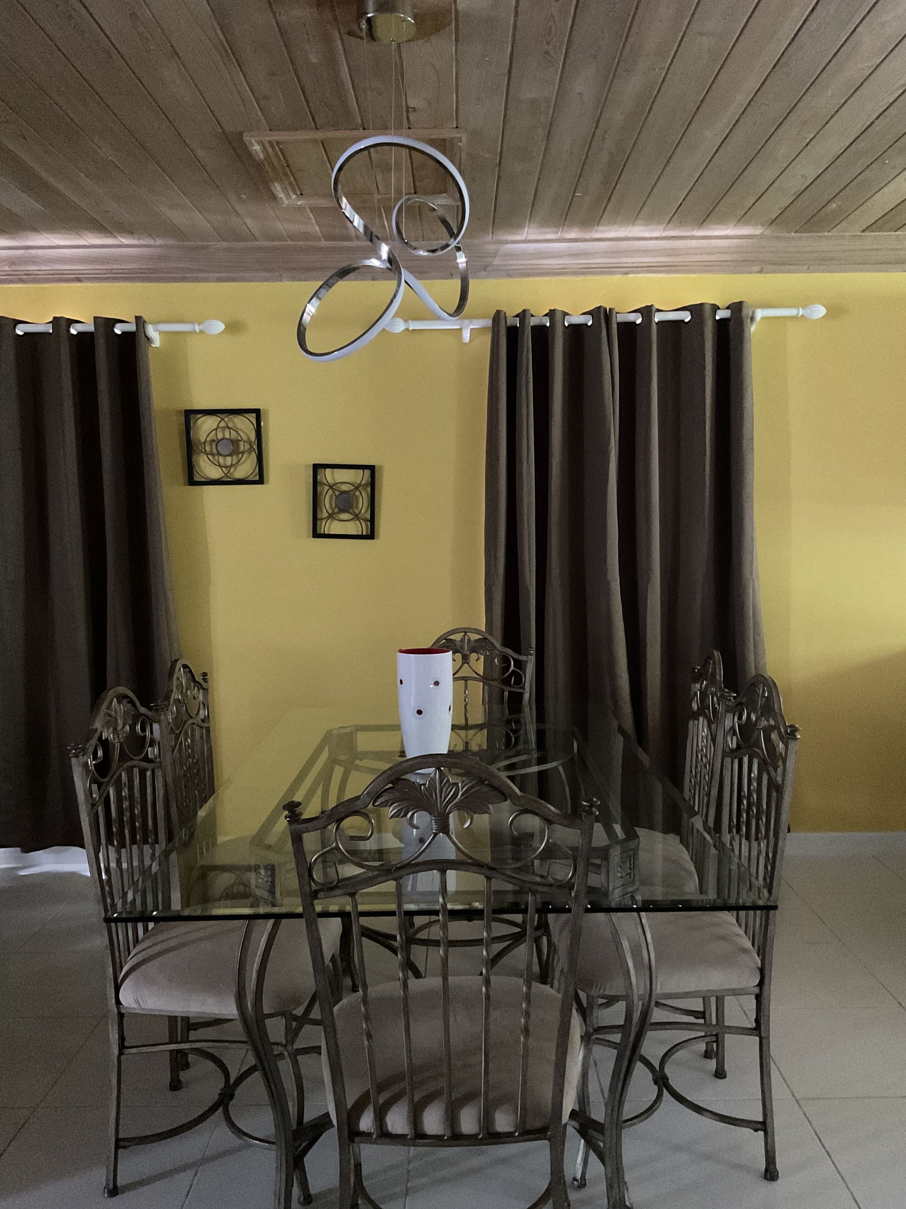 A dining area with a glass table surrounded by metal chairs, a ceiling fan, and curtains.
