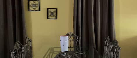Un espace repas avec une table en verre entourée de chaises en métal, un ventilateur de plafond et des rideaux.