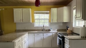 A kitchen with white cabinets, a granite countertop, a window, and a stove. - Sapphire Garden Townhouses (George Town)