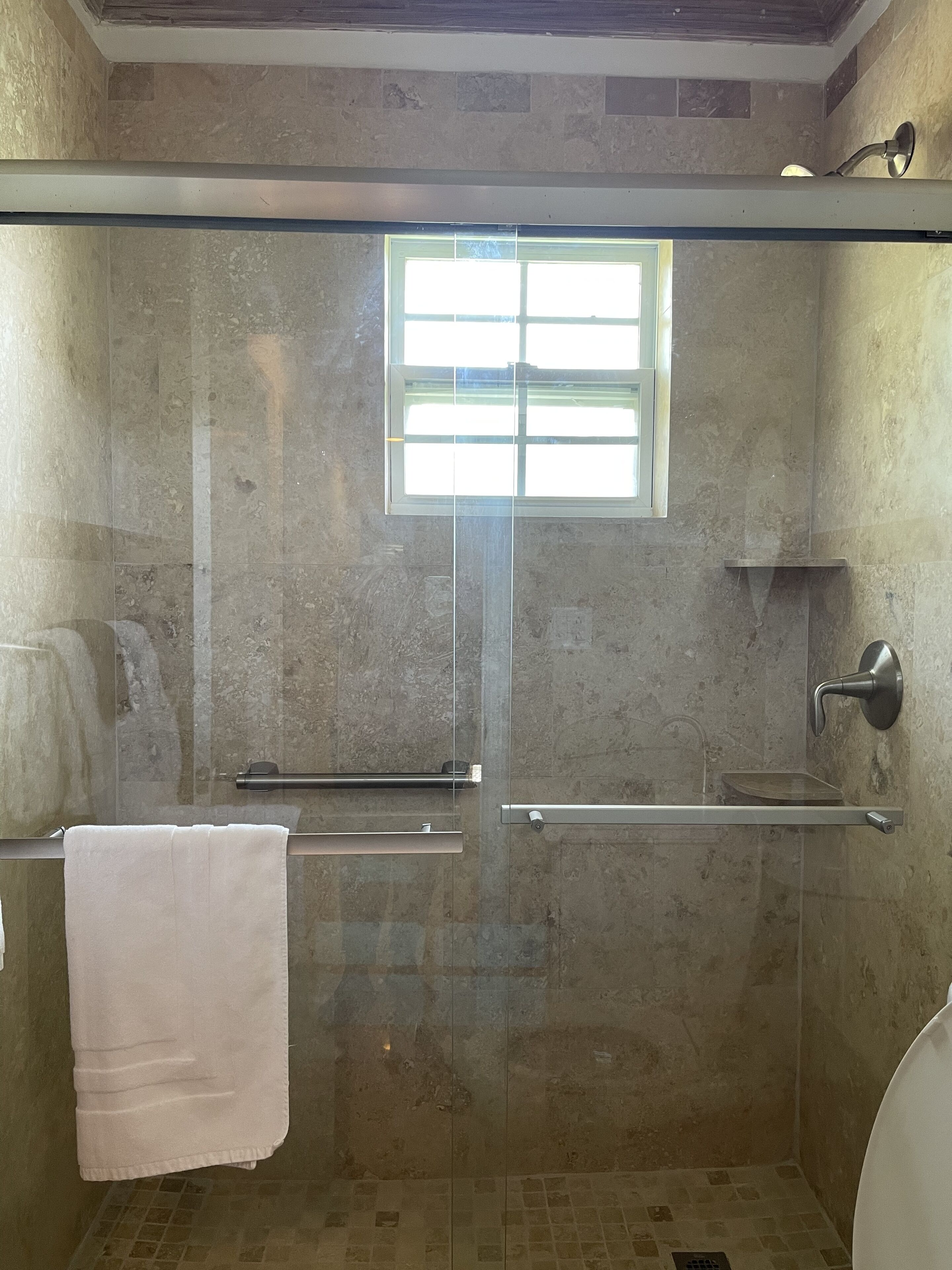 A glass-enclosed shower with a window, a towel rack, and a sink.