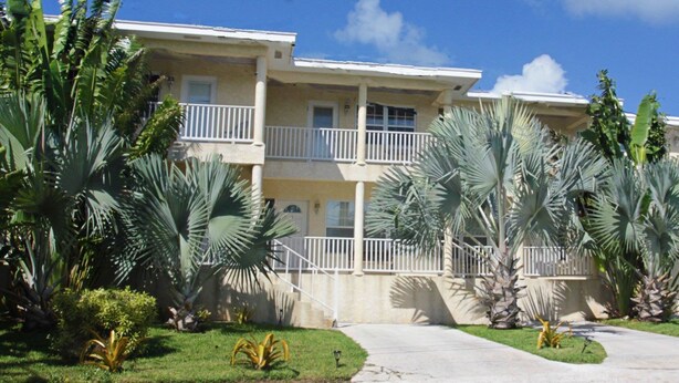 A multi-story residential building with balconies, surrounded by tropical plants and a clear blue sky. - Sapphire Garden Townhouses (George Town)