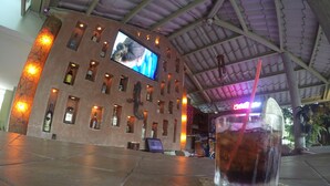 Un coin bar avec un écran de télévision, des bouteilles d’alcool et un verre posé sur une table.