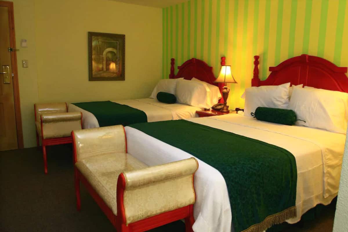 A hotel room with two beds, a chair, a lamp, and a painting on the wall.