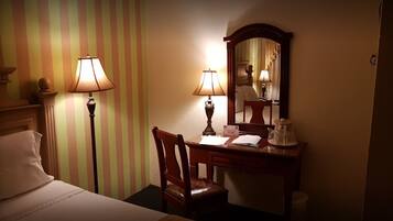 Habitación de hotel con cama, escritorio y silla, dos lámparas, un espejo y mesita de noche con jarra.