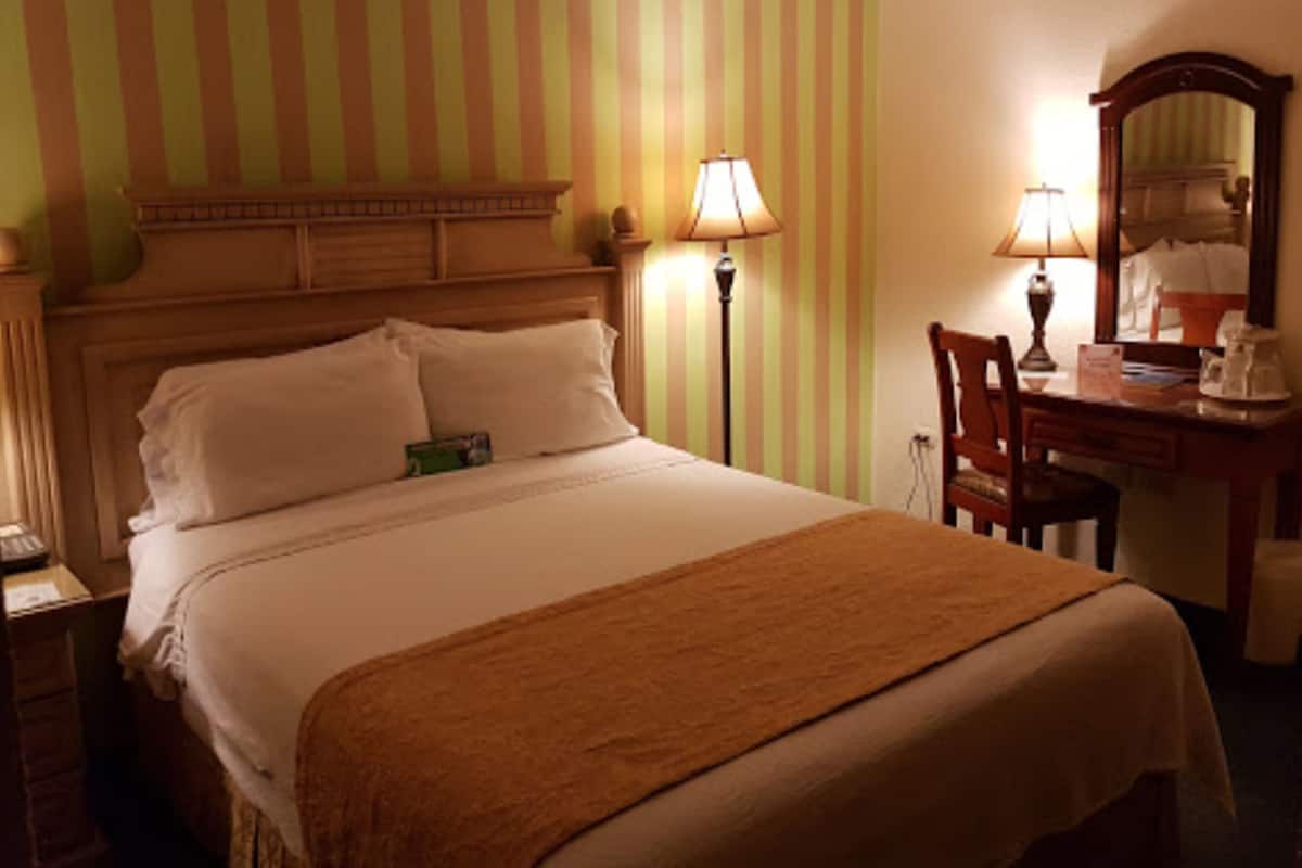 A hotel room with a large bed, a desk with a chair, a lamp, and a mirror.