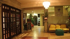 Un hall d’hôtel comprenant un comptoir d’accueil, un canapé, un pouf vert et un lustre.