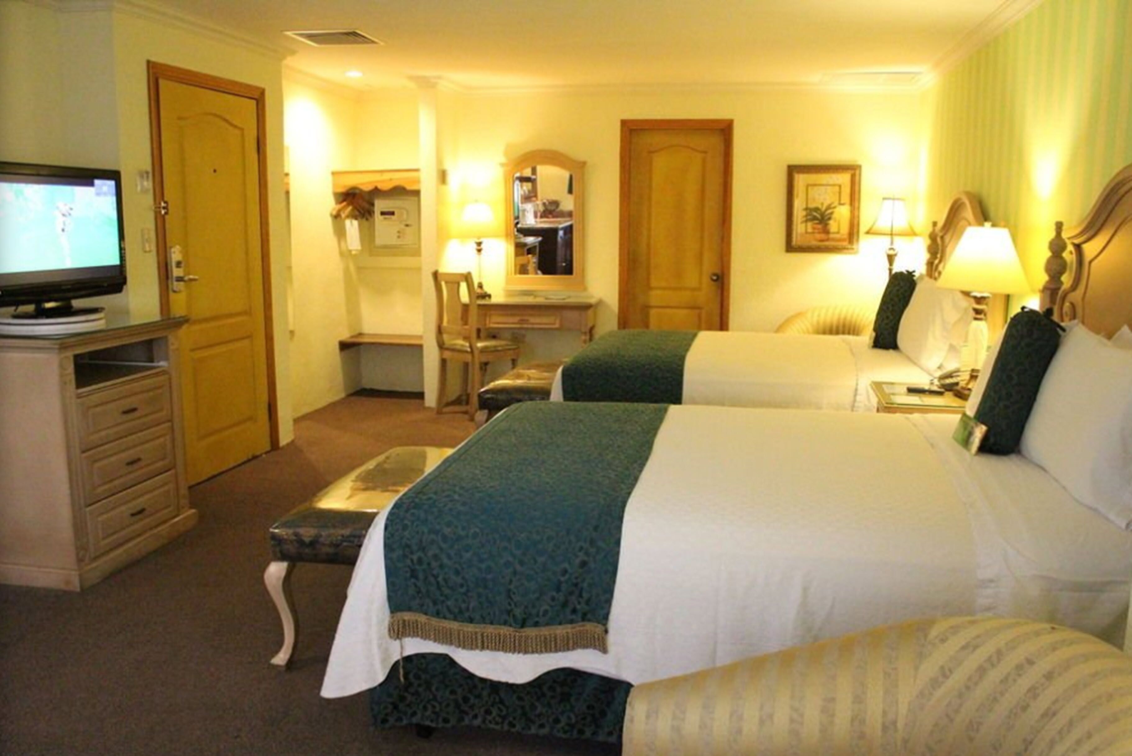 A hotel room with two beds, a desk, a chair, a television, and lamps.