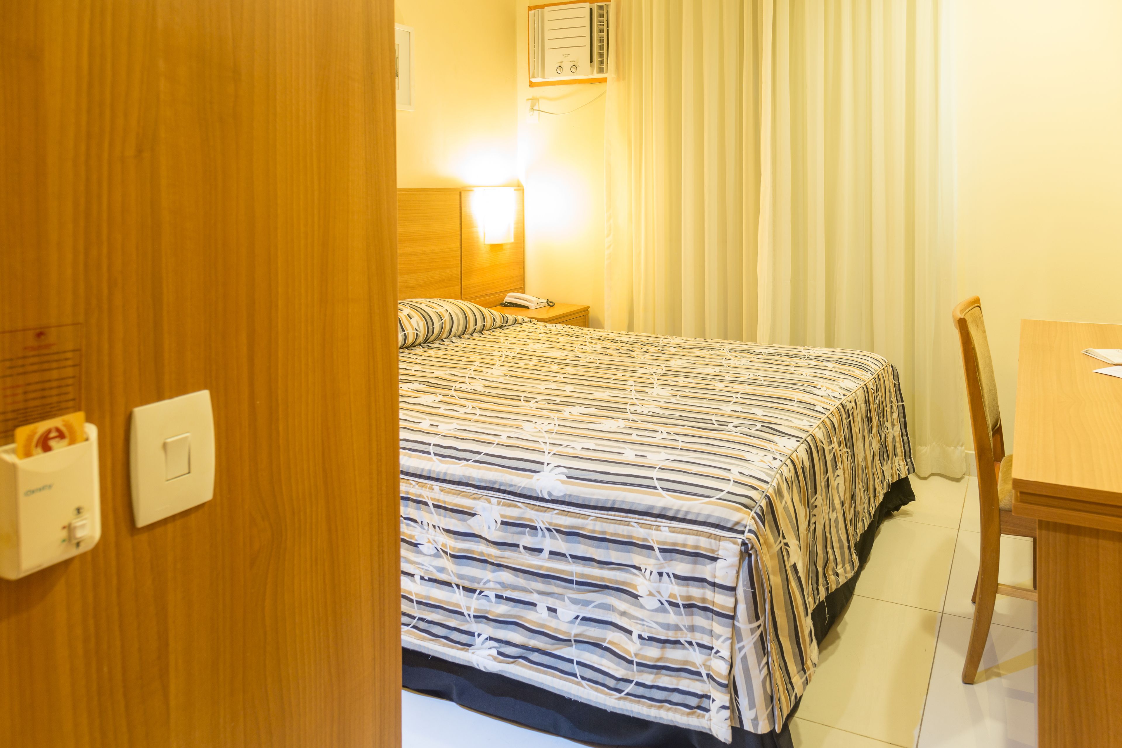 Une chambre d’hôtel avec un lit, une table de chevet, une lampe et une chaise en bois.