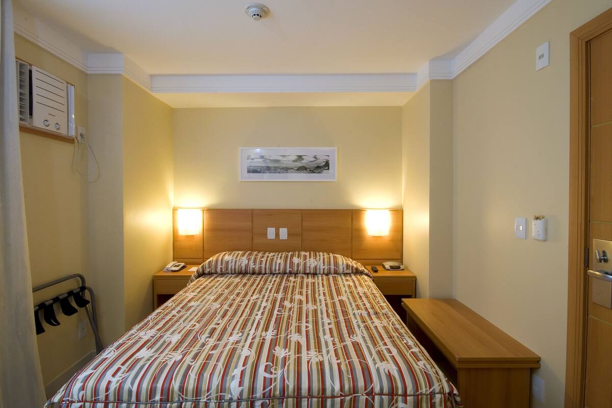 Een hotelkamer met een bed, nachtkastjes, een houten bankje, een hangend schilderij en een wandradiator.