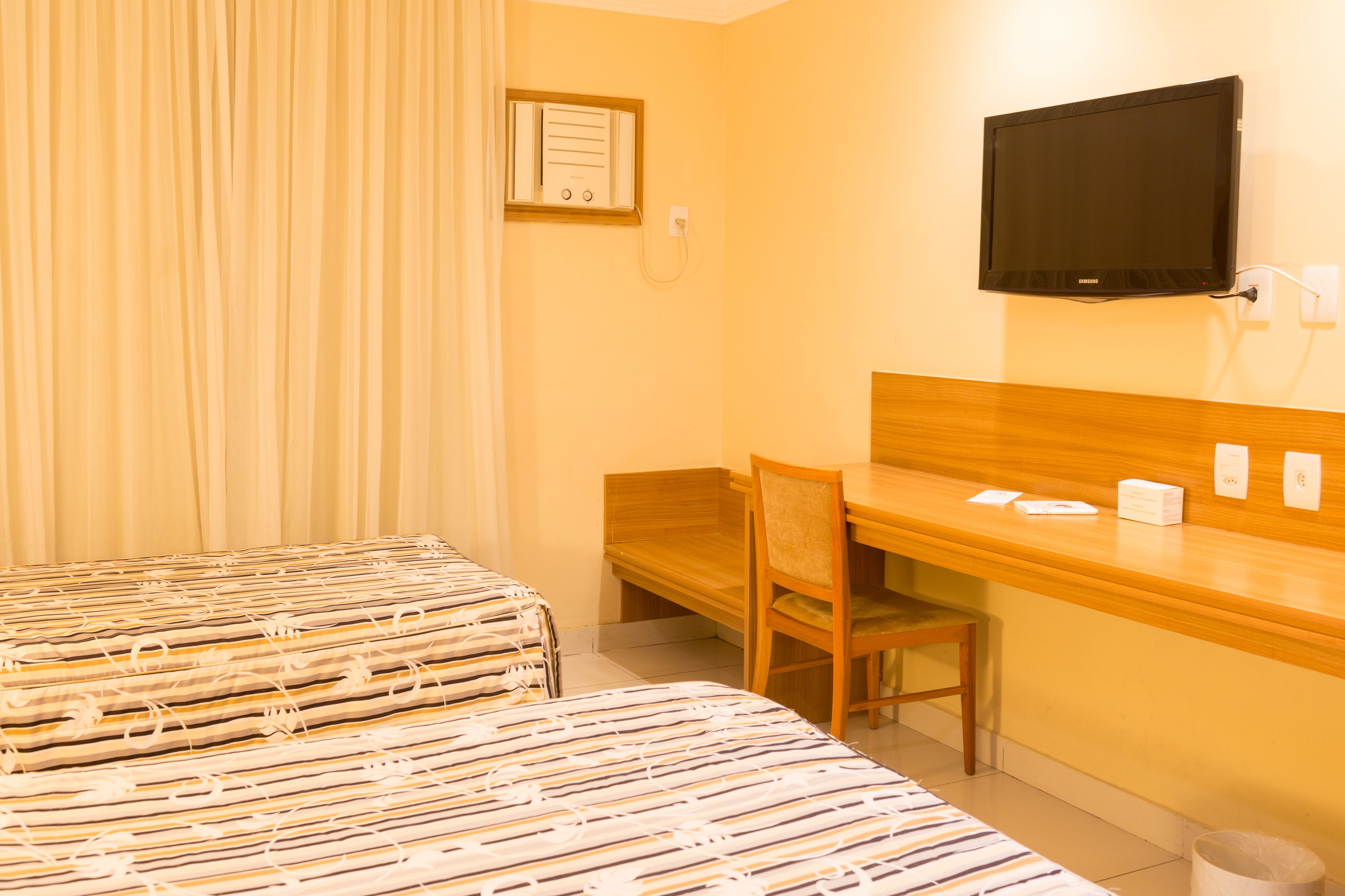 A hotel room with two beds, a desk, a chair, a television, and a window with curtains.