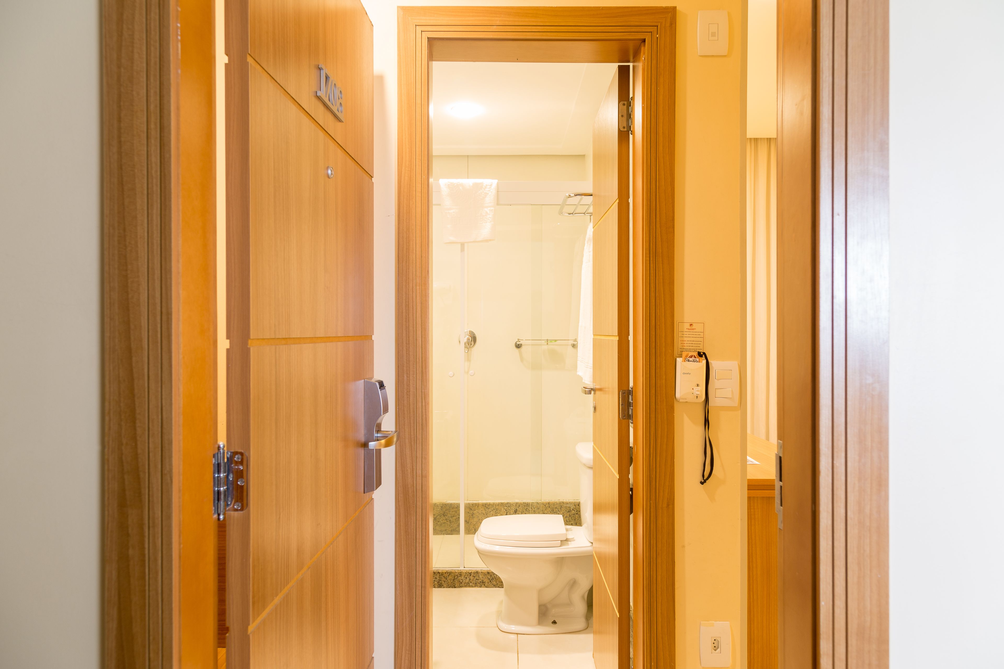 A wooden door leading to a bathroom with a toilet, shower, and a towel rack.