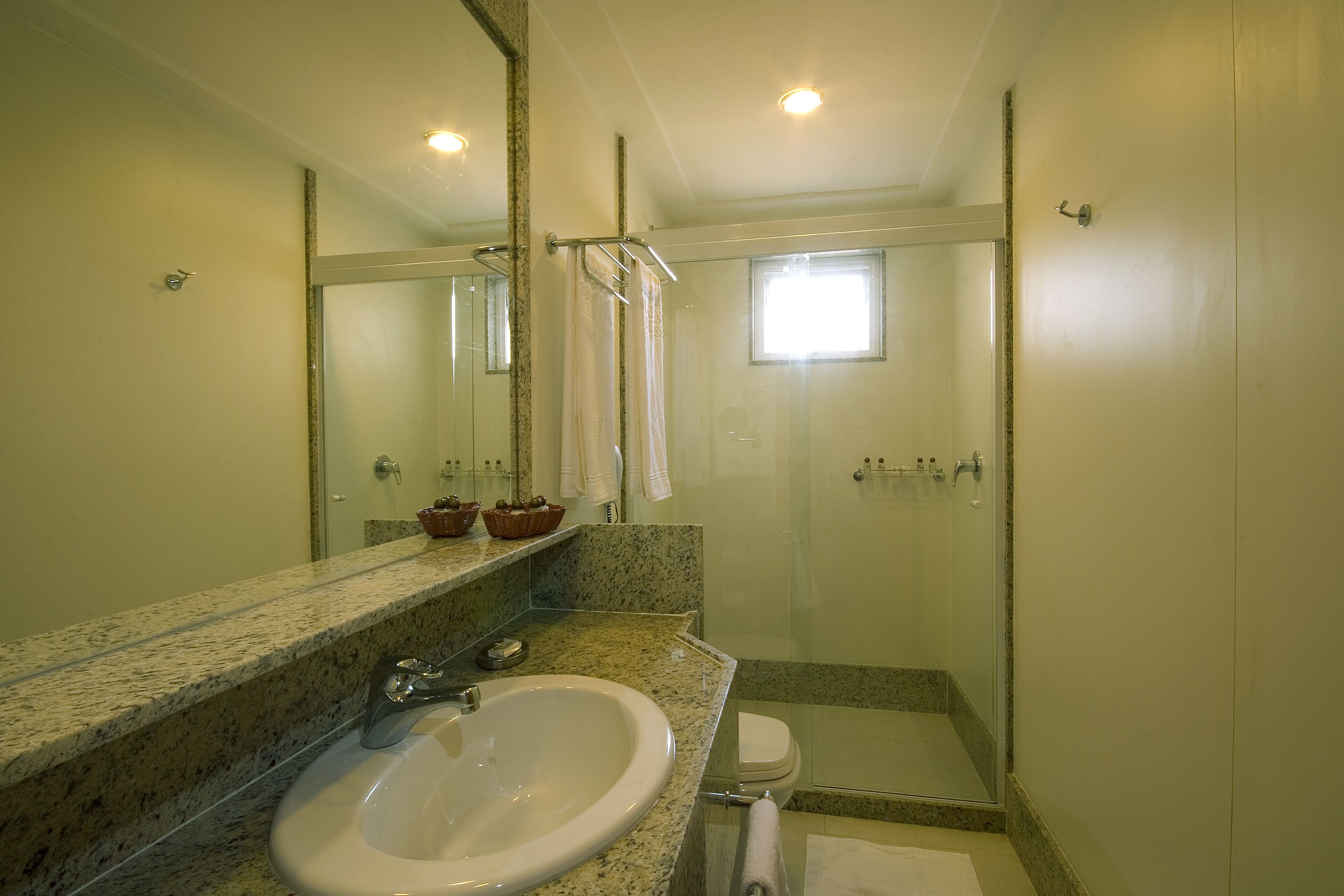 Une salle de bain avec un comptoir en granit, un lavabo blanc, une cabine de douche en verre et une petite fenêtre.