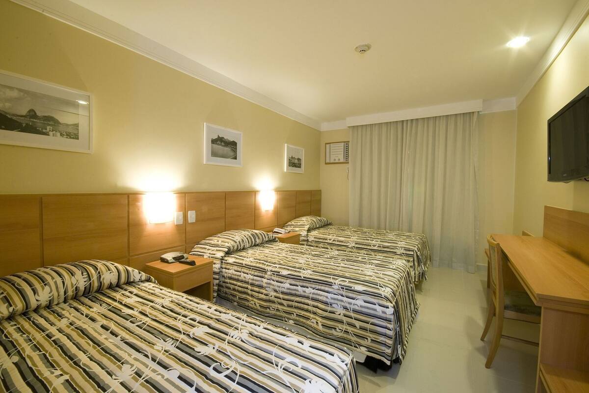 Een hotelkamer met twee bedden, een bureau, een televisie en lijstjes met foto’s aan de muur.
