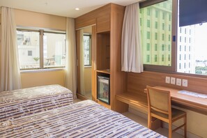 Een hotelkamer met twee bedden, een bureau en uitzicht op een gebouw.