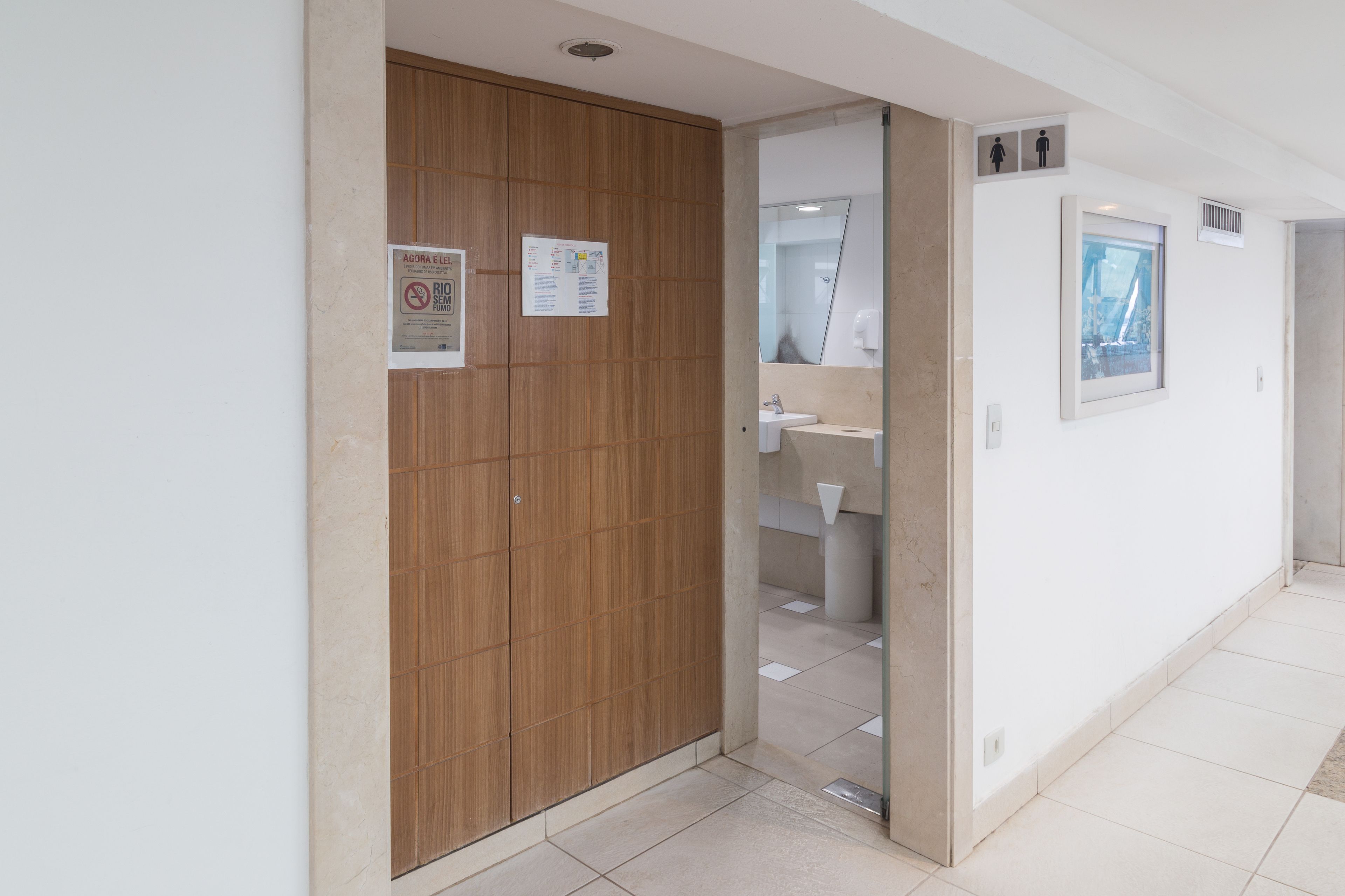 A hotel room with a wooden wardrobe, a bathroom with a sink and mirror, and a window with a view.