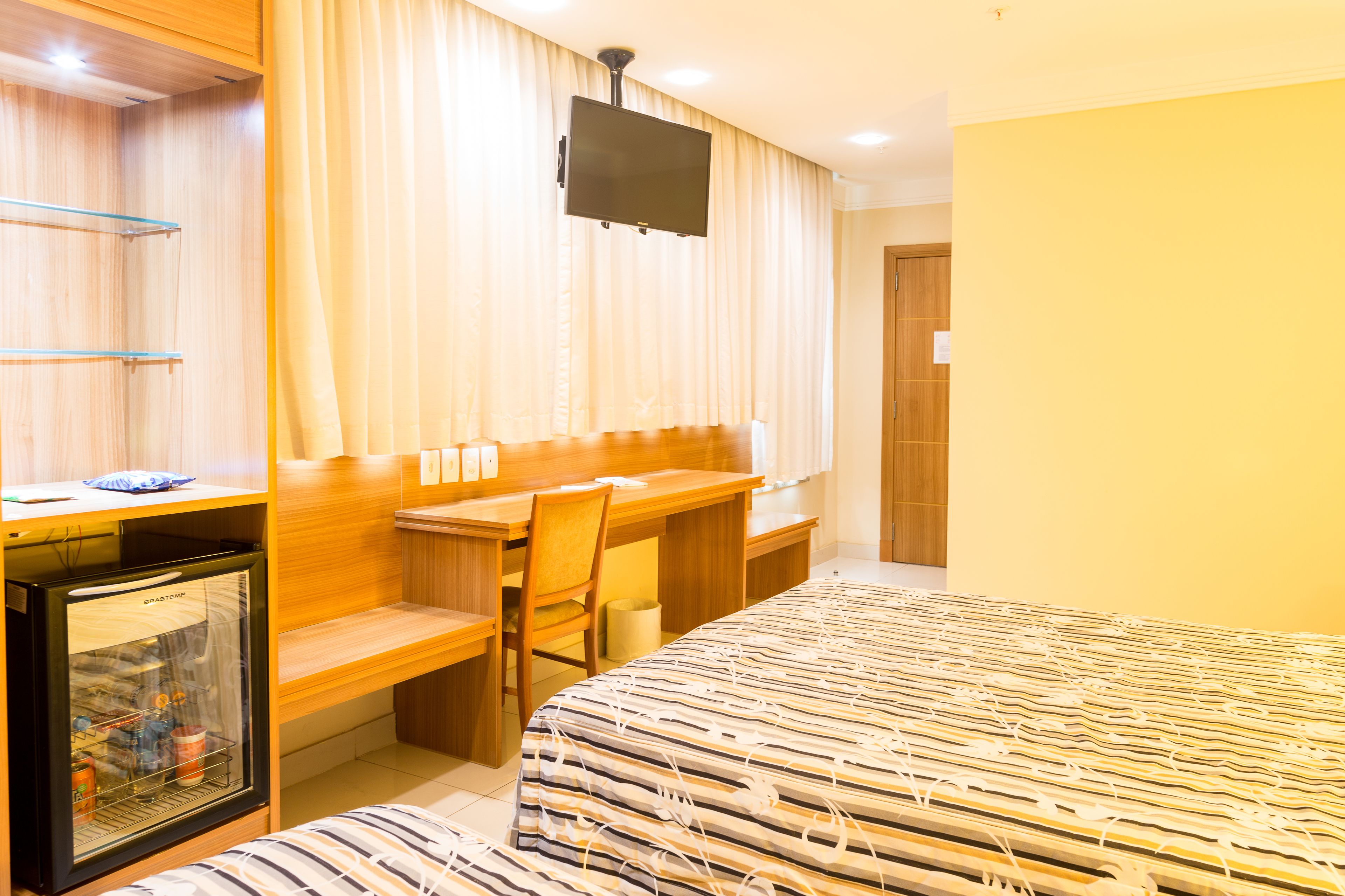 A hotel room with a bed, a desk, a chair, a television, and a minibar.