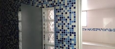 A bathroom with a tiled wall featuring a blue and white pattern, a white door, and a window with a view of the outside.