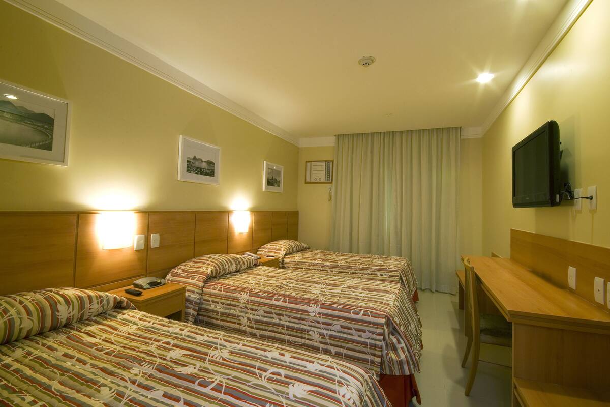 Een hotelkamer met drie bedden, een bureau en een televisie.