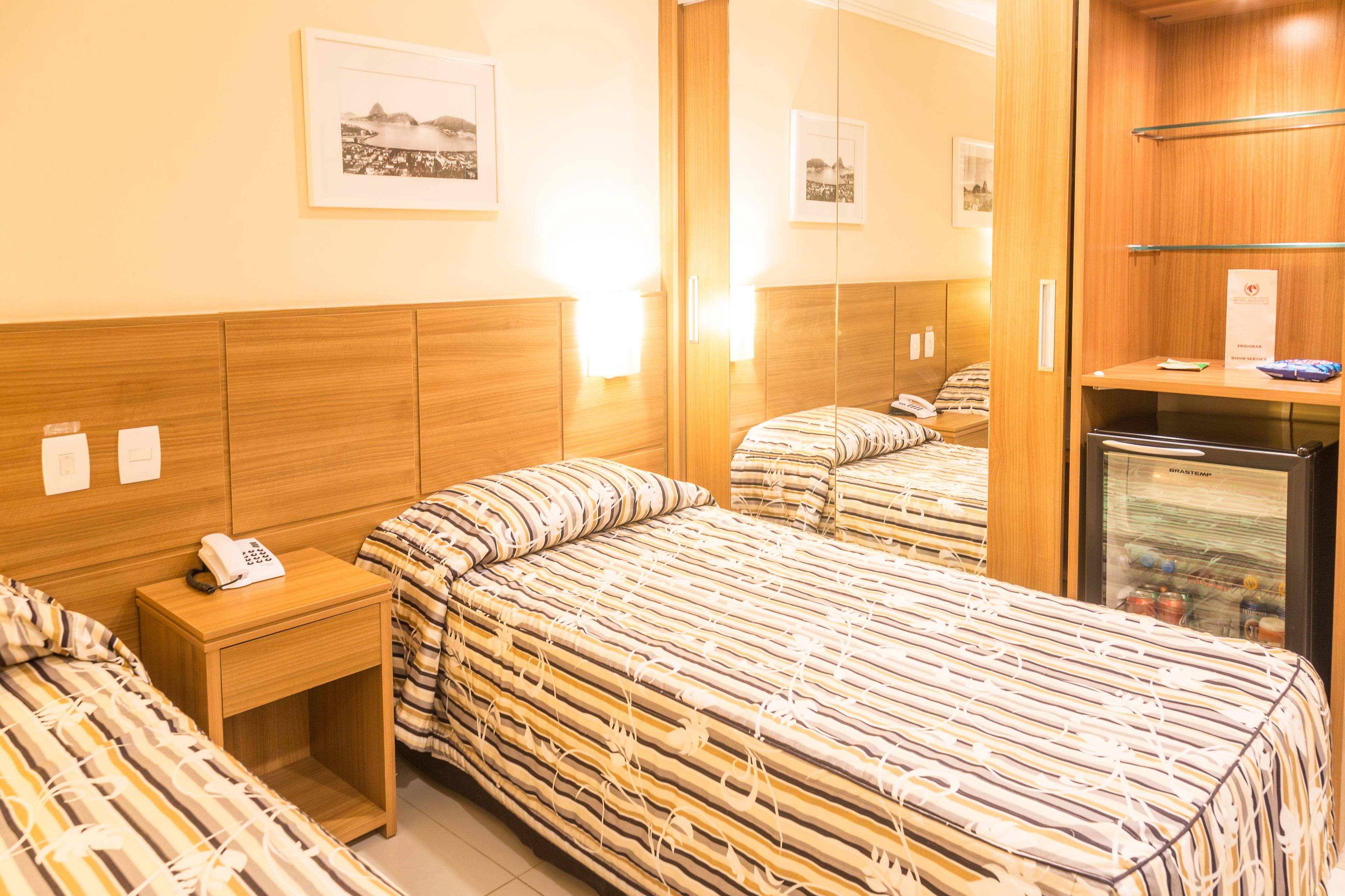 Une chambre d’hôtel avec une tête de lit en bois, une table de chevet avec un téléphone et un lit avec une literie à rayures.