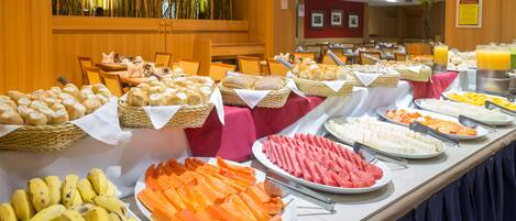 Un bufé con diversas opciones de comida, incluyendo frutas, pan y pasteles.