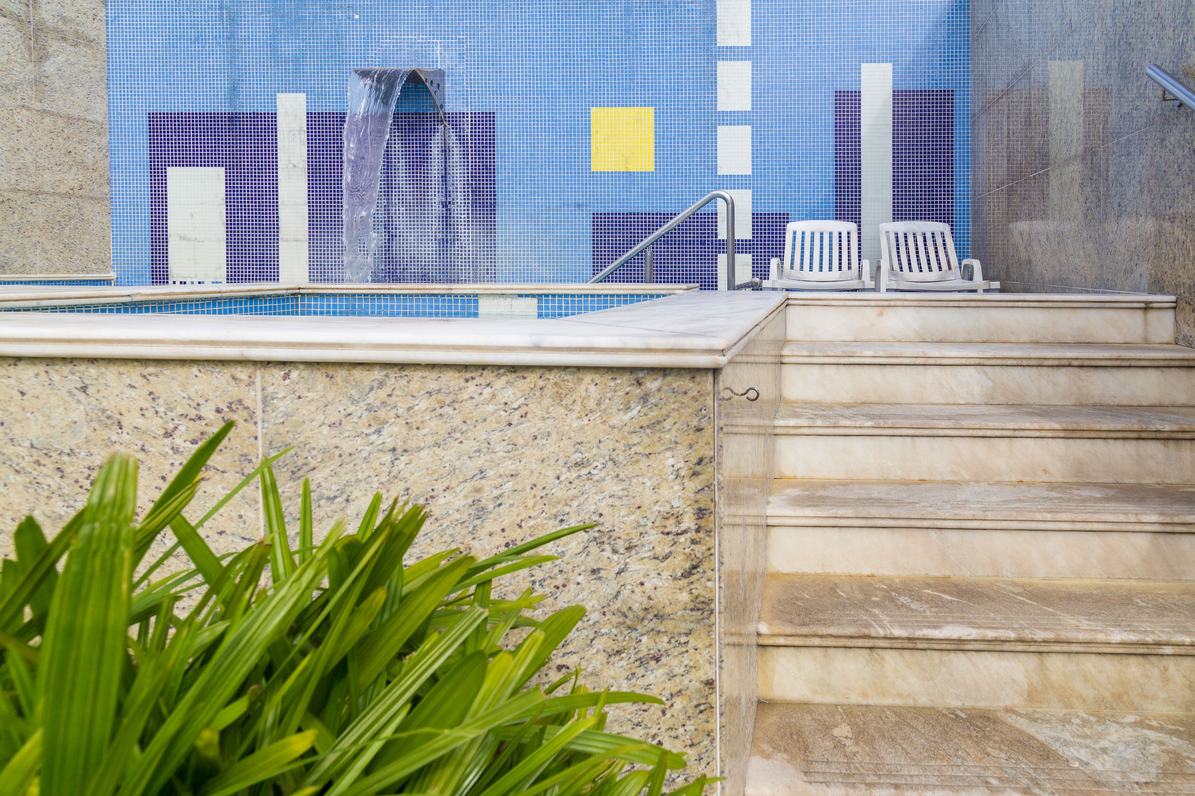 A pool area with steps leading down to the water, a tiled wall, and a chair.
