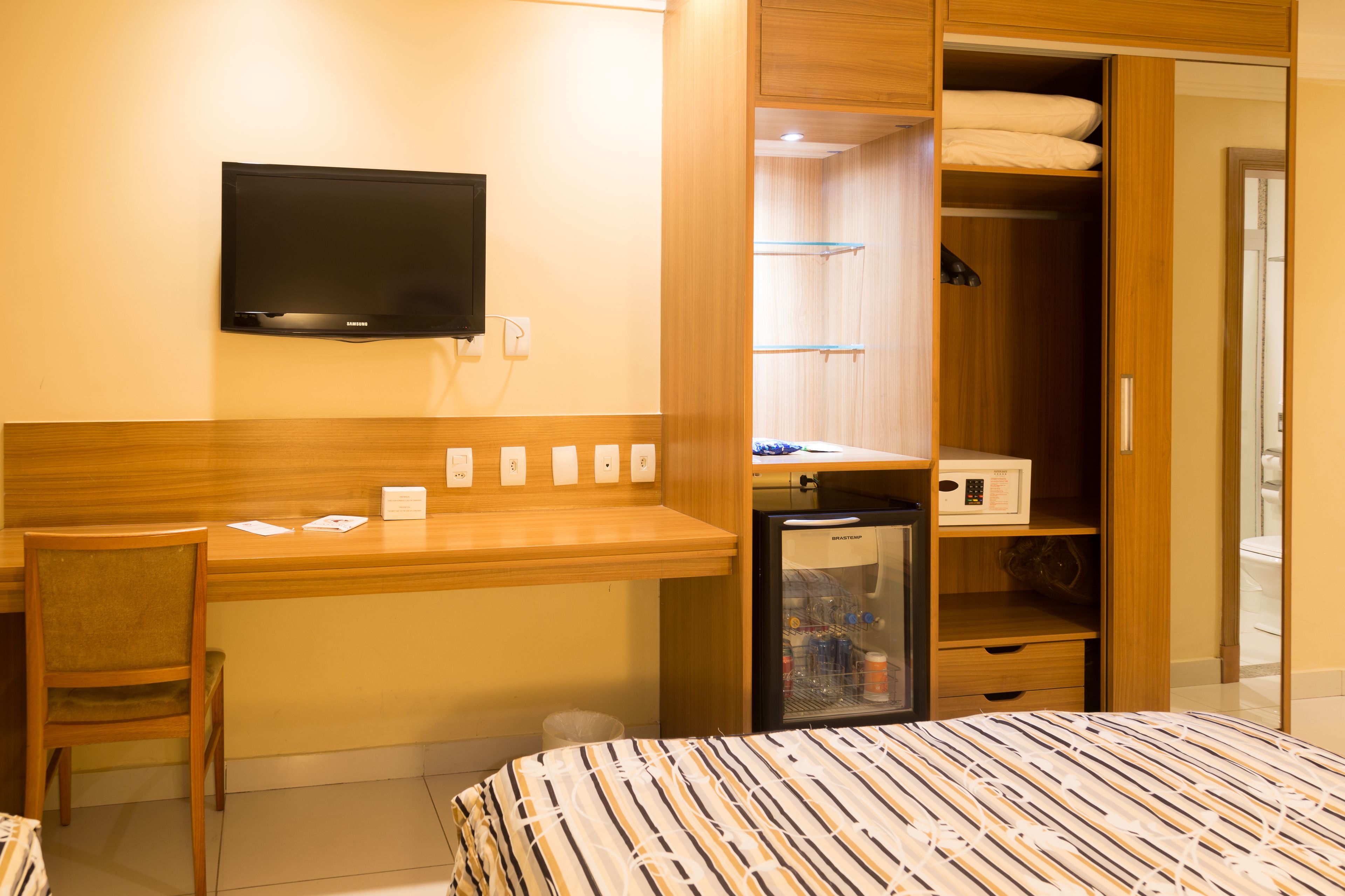 Habitación de hotel con cama, escritorio, silla, televisor, minibar y armario.