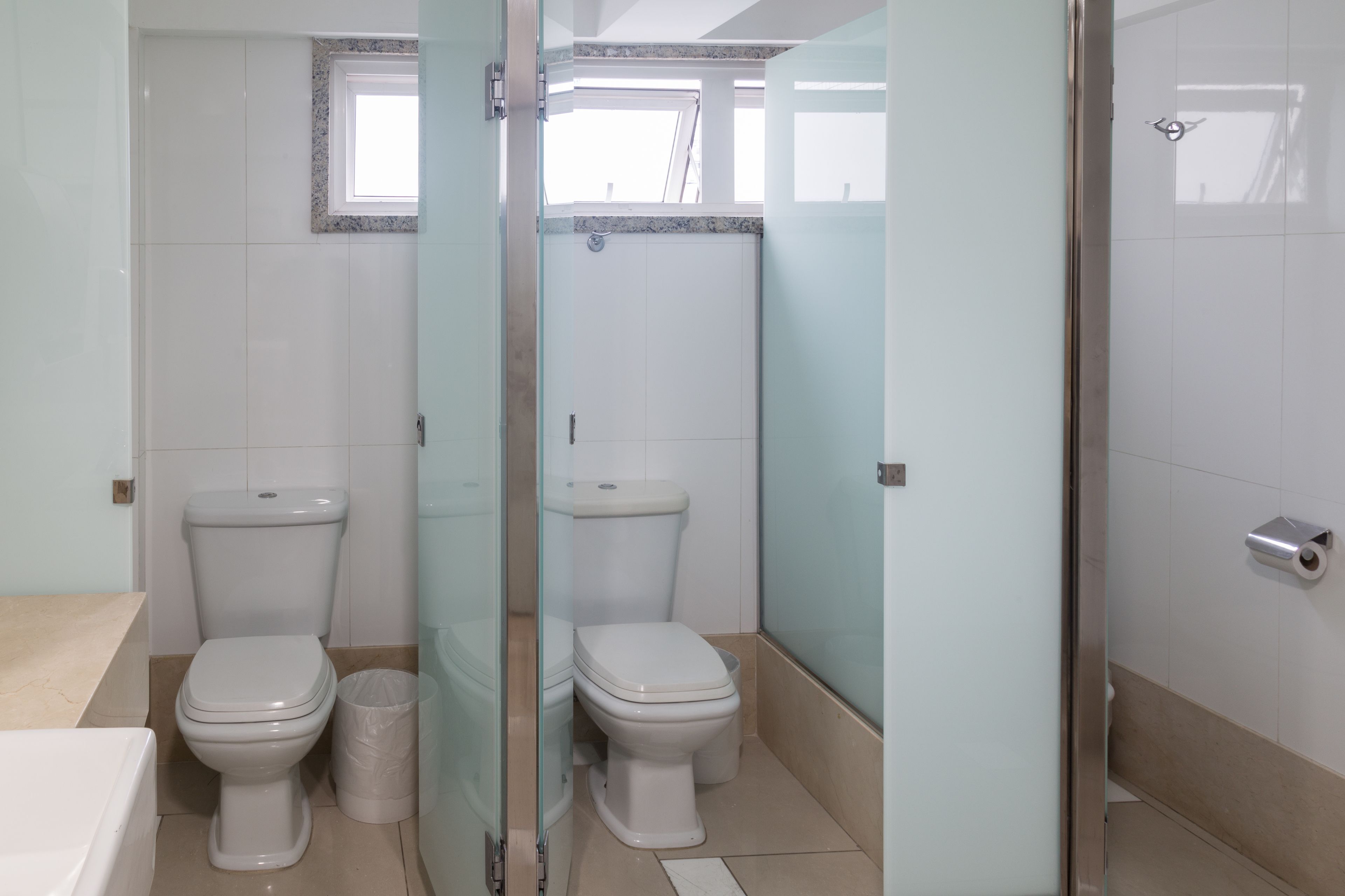 Baño con dos inodoros, cabina de ducha de vidrio y ventana.