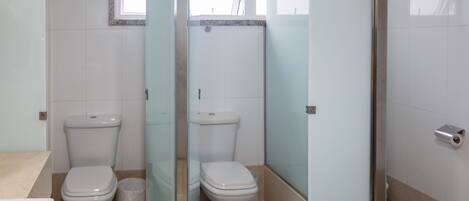 Baño con dos inodoros, cabina de ducha de vidrio y ventana.