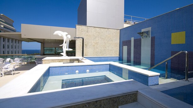 Une piscine sur le toit, avec des carreaux bleu clair, une sculpture blanche et un bâtiment moderne doté d’une façade en verre.