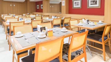 Un espace repas comprenant plusieurs tables et chaises, chaque table étant dressée avec de l’assiette blanche, des tasses et des couverts.