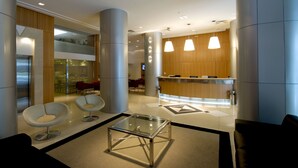 Un hall d'entrée moderne avec un comptoir de réception, deux tables à plateaux en verre et des sièges contemporains.