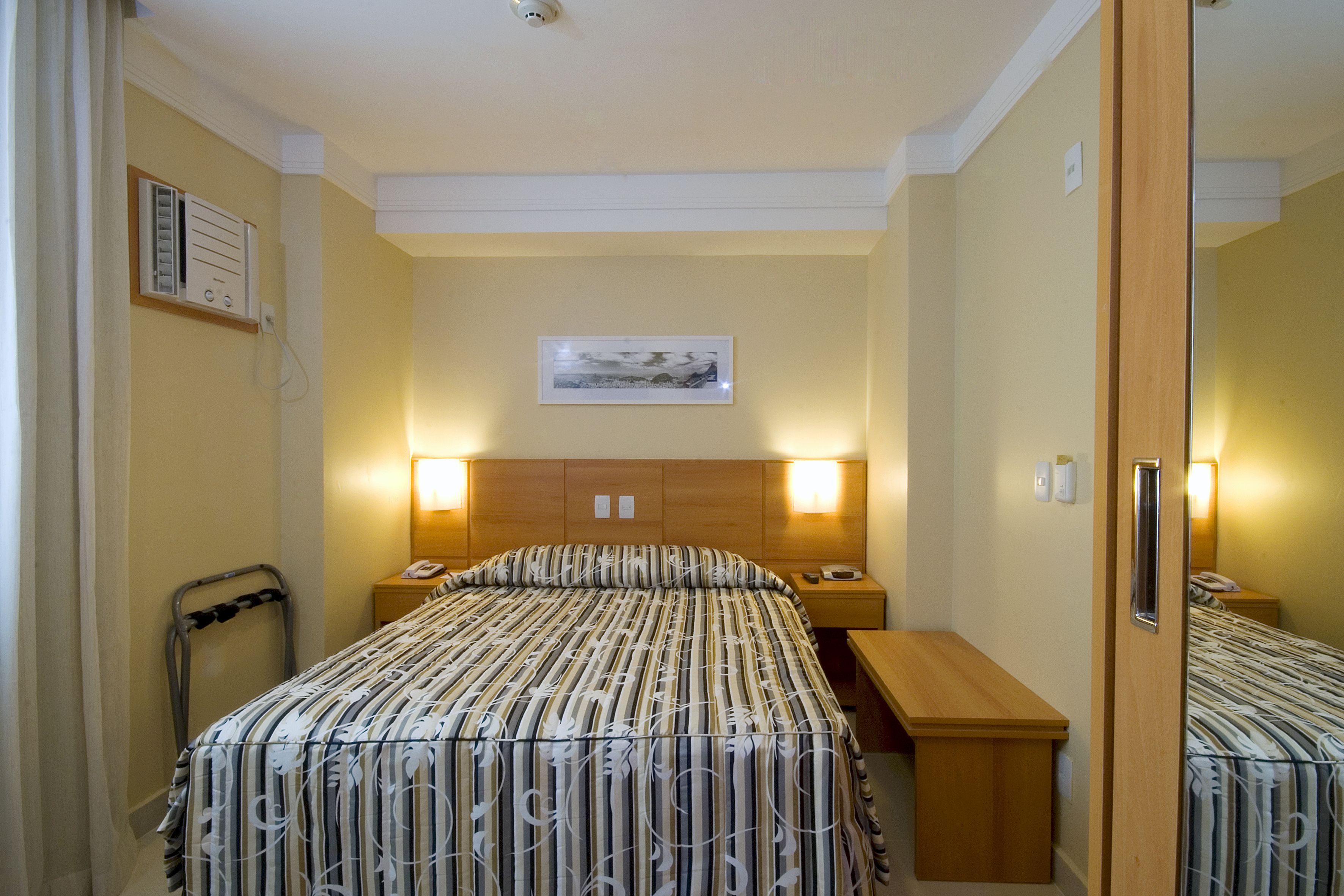 Une chambre d’hôtel avec un lit, des tables de chevet, un bureau, une chaise, un miroir et un tableau au mur.