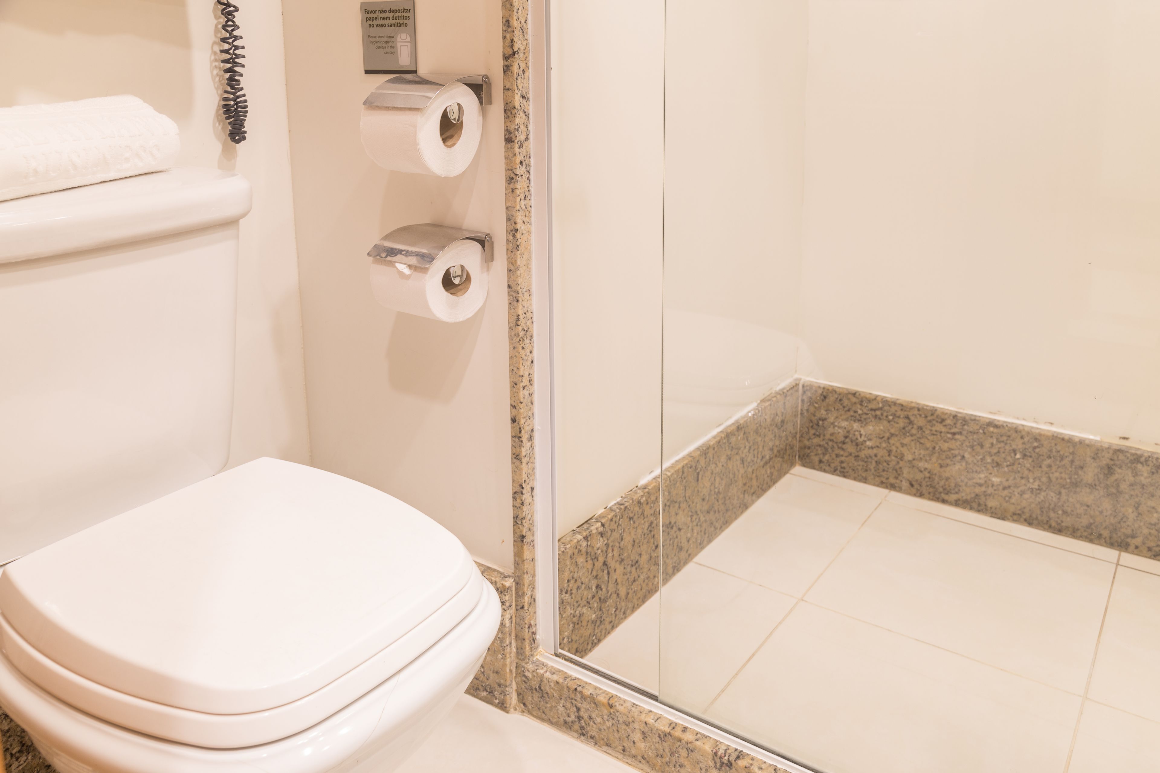 Une salle de bain comprenant des toilettes, un espace douche doté d’une porte en verre et un porte-serviettes avec une serviette.