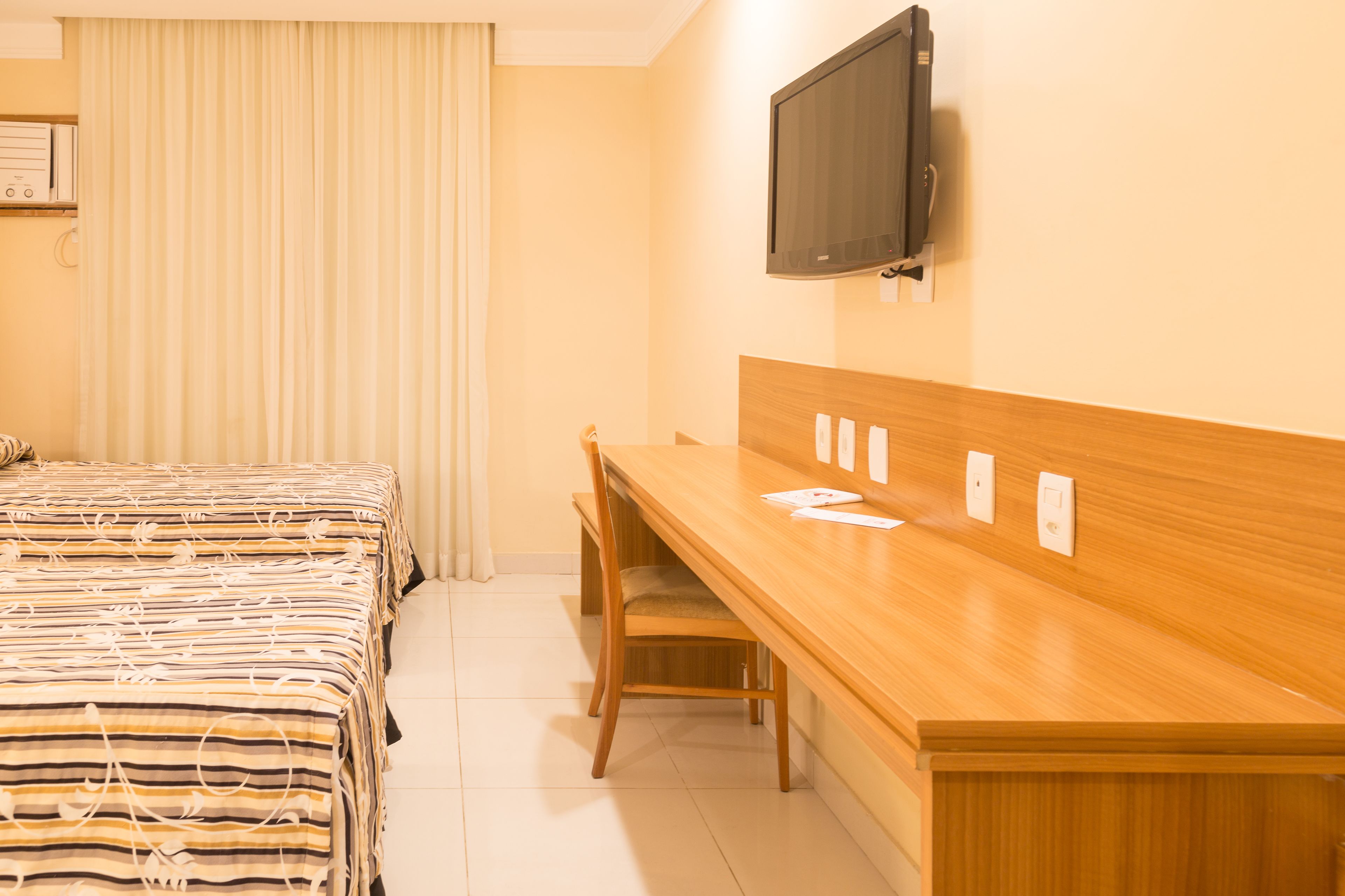 A hotel room with a bed, a desk, a chair, a television, and a window with curtains.