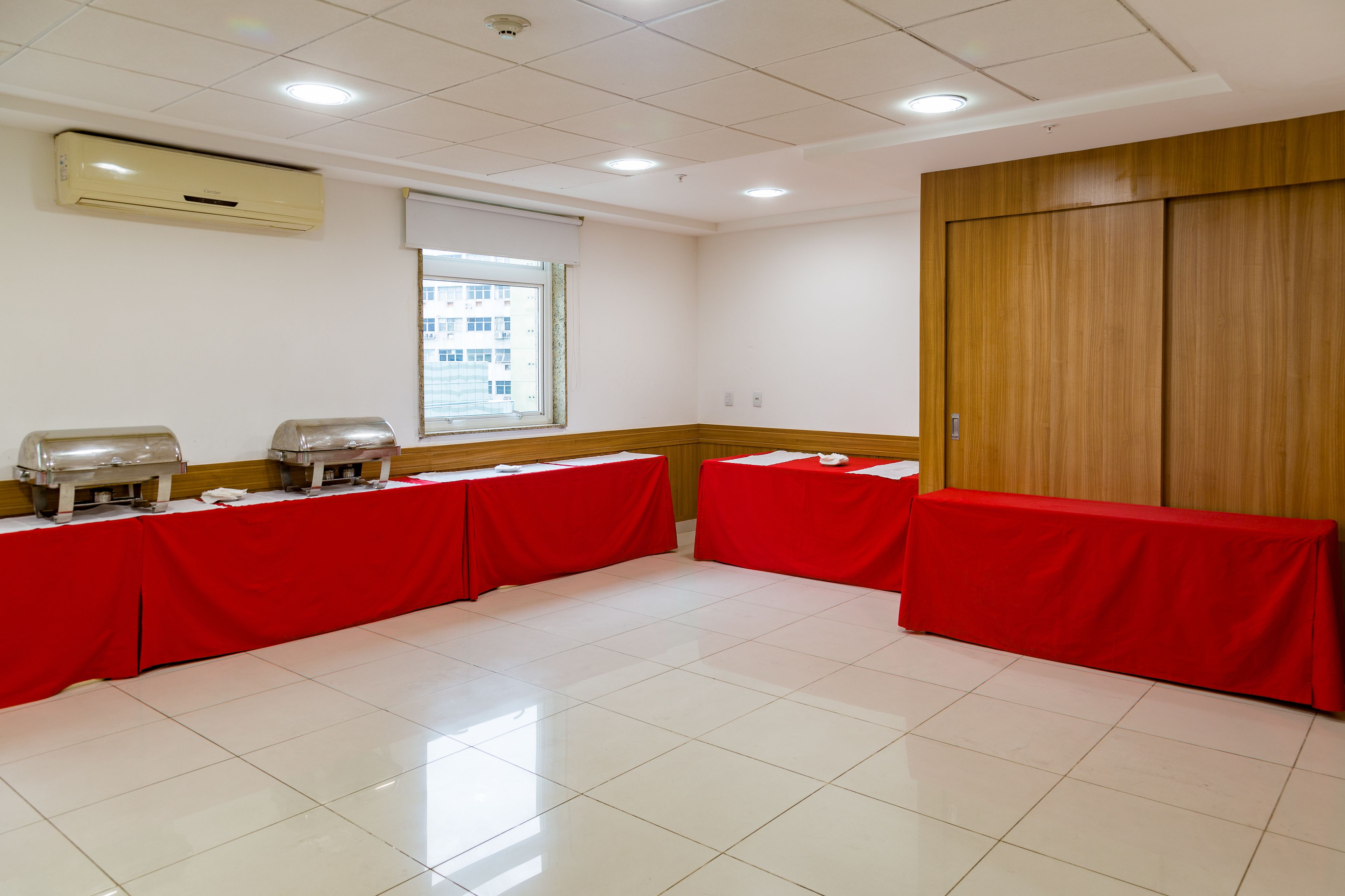 A conference room with a tiled floor, red tablecloth-covered tables, and a wooden wardrobe.